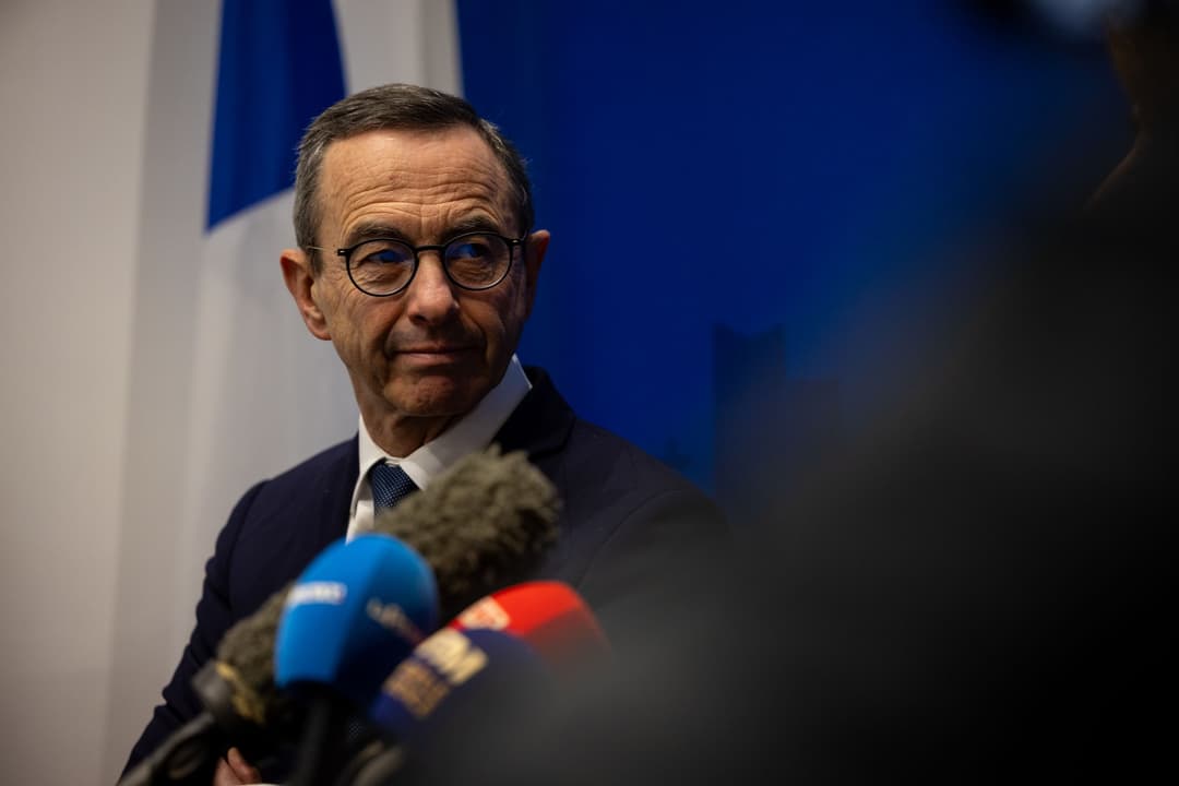 Bruno Retailleau face aux micros de la presse, devant un drapeau tricolore